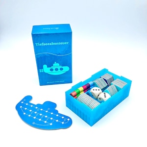 Può includere: Una scatola blu con il testo "Tiefseeabenteuer" e un sottomarino dei cartoni animati sul davanti. La scatola contiene un tabellone di gioco, carte e dadi. Il tabellone di gioco è un sottomarino blu con una pista numerata.