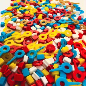 May include: A vibrant assortment of colorful plastic game pieces in red, yellow, blue, white, and gold. The pieces include key-shaped, rectangular, and ring-shaped components, creating a playful and visually appealing mix.