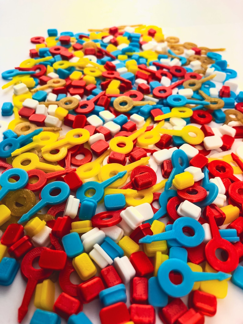 May include: A vibrant assortment of colorful plastic game pieces in red, yellow, blue, white, and gold. The pieces include key-shaped, rectangular, and ring-shaped components, creating a playful and visually appealing mix.