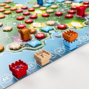 Könnte beinhalten: Ein Brettspiel mit einer Landkarte aus hexagonalen Geländefeldern, kleinen Kunststoffburgen in Rot, Orange, Beige und Blau sowie verschiedenen farbigen Spielsteinen. Das Spielfeld enthält eine nummerierte Leiste entlang blauer Wasserflächen.