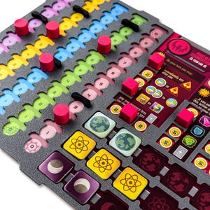 Könnte beinhalten: Ein Spielbrett-Komponente mit grauem Grund, mit farbigen Schlitzen und Holzteilen. Das Spielbrett hat verschiedene Symbole und Text, darunter "PHOENIX FOUNDATION TECH LAB". Es gibt rosa, gelbe, grüne und blaue Elemente.