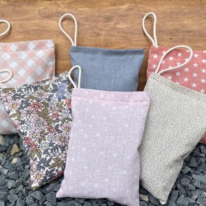 Può includere: Una collezione di piccoli sacchetti di stoffa in vari modelli e colori. I disegni includono rosa a quadretti, floreale, blu, rosa con stelle bianche e grigio con pois bianchi. Ogni sacchetto ha un anello bianco.