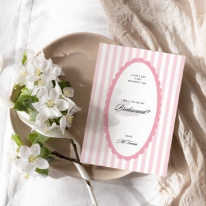May include: Pink and white striped card with a scalloped pink oval frame. The text inside the frame reads "I can't say 'I do' without you. Will you be my Bridesmaid? XOXO [Name]".