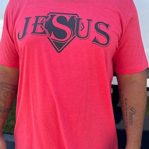 May include: Red t-shirt with a black Superman-style logo that says "JESUS" in a bold font.