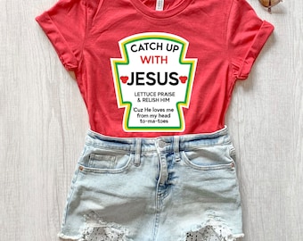 May include: Red t-shirt with a ketchup-style graphic that says "Catch Up With Jesus." The graphic has a red tomato and green lettering. The text below the graphic says "Lettuce Praise & Relish Him 'Cuz He loves me from my head to-ma-toes."