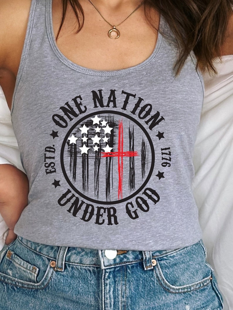 May include: Gray tank top with a black and white American flag design and a red cross. The text "ONE NATION UNDER GOD ESTD. 1776" is printed around the flag.