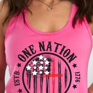 May include: Pink tank top with a black and white graphic of an American flag with a red cross in the center. The graphic is in a circle with the text "One Nation Under God" and "Estd. 1776" around the circle.