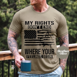 May include: A khaki t-shirt with a black and white graphic of an American flag with guns superimposed on it. The text "My Rights Don't End Where Your Feelings Begin" is printed on the shirt.