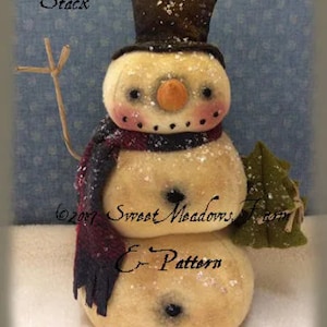 May include: A snowman stack with a black top hat, red and black scarf, and a green leafy branch. The snowman is made of white fabric and has a brown nose and black eyes. The text "Snowman Stack" is written above the snowman and "Sweet Meadows Farm E-Pattern" is written below the snowman.