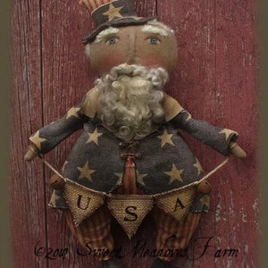 May include: A handmade rag doll dressed in a blue and white star patterned fabric with red and white striped accents. The doll is wearing a red, white, and blue striped hat and holding a banner that says "USA".