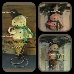 May include: Three handmade snowman ornaments, each with a green scarf and a red candy cane. The snowmen are made of fabric and are attached to a metal spring. The snowmen are on a wooden background with the text "2015 Sweet Meadows Farm".