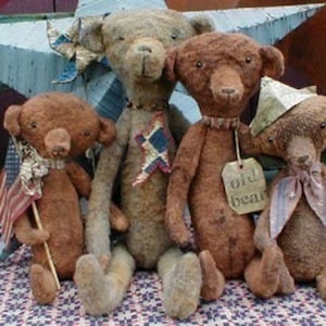 May include: Four brown teddy bears with different fabric textures and accessories. One bear is holding a small American flag, another has a tag that says "Old Bear", and another is wearing a blue and white patterned ribbon. The bears are sitting on a red, white, and blue patterned fabric.