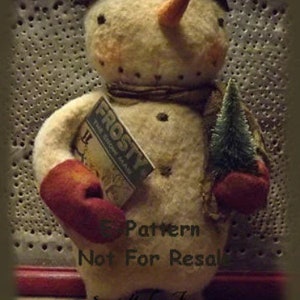 Op de afbeelding: Een handgemaakte vilten sneeuwpoppop met een zwarte hoed, een rode want en een kleine groene boom. De sneeuwpop houdt een boek vast met de titel "Frosty The Snowman". De pop staat op een houten voet. 5 Pattern Not For Resale. Sweet Meadows Farm.