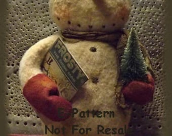 May include: A handmade felt snowman doll with a black hat, a red mitten, and a small green tree. The snowman is holding a book titled "Frosty The Snowman". The doll is standing on a wooden base. 5 Pattern Not For Resale. Sweet Meadows Farm.