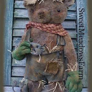 May include: A brown teddy bear dressed as a scarecrow with a straw hat, overalls, and green gloves. The bear is holding a small brown mouse in its arms. The bear is standing on a wooden surface. The text "Sweet Meadows Farm" is visible in the background.