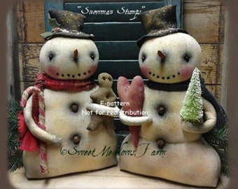 May include: Two handcrafted snowman figures with black top hats, holding a gingerbread man and a heart. One snowman wears a red scarf. The text "Snowman Stamps" is above them. The bottom text says "Sweet Meadows Farm".