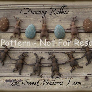 May include: A string of dancing rabbit ornaments with painted details, holding hands and decorated with Easter eggs. The banner reads "Dancing Rabbits" and "E-Pattern - Not For Resale" and "2012 Sweet Meadows Farm".