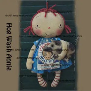 May include: A handmade rag doll with red hair, wearing a blue and white dress with a pig design and the text "Praw Hog Wash". The doll is holding a small pig in its arms.