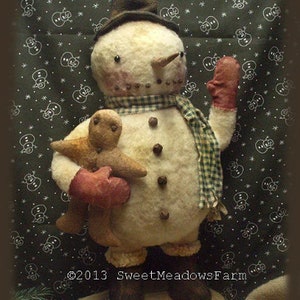 May include: A handmade felt snowman doll holding a gingerbread person. The snowman is wearing a plaid scarf and a brown hat. The background is a green fabric with white snowflakes.