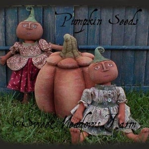 Peut inclure: Deux poupées faites à la main en forme de citrouille avec des visages peints et des robes fleuries. Les poupées sont debout devant une clôture en bois avec le texte "Pumpkin Seeds" écrit dessus.