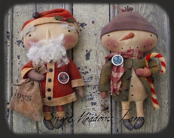 May include: Two handmade rag dolls, one dressed as Santa Claus with a sack of toys and the other as a snowman with a candy cane. Both dolls have a rustic, vintage style.