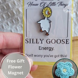 May include: A white and yellow enamel pin of a goose wearing a sunflower, with the text "SILLY GOOSE Energy." The pin is on a yellow backing card with the words "House Of Little Things." A free flower magnet is included.