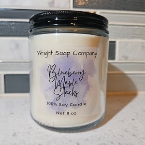 May include: A glass jar candle with a white label that reads "Wright Soap Company", "Blueberry Maple Stacks", "100% Soy Candle", and "Net 8 oz".