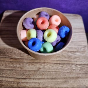 May include: A brown paper bowl filled with colorful donut-shaped wax melts. The wax melts are in shades of blue, green, orange, pink, and purple.