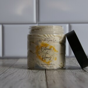 K&ouml;nnte beinhalten: Ein Glasgef&auml;&szlig; mit geschlagenem K&ouml;rperbutter und einem schwarzen Deckel. Das Gef&auml;&szlig; hat ein Etikett mit der Aufschrift "Wight Soap Co. Oatmeal & Honey Whipped Body Butter 2.5 oz / 70 Gramm".