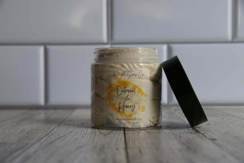 K&ouml;nnte beinhalten: Ein Glasgef&auml;&szlig; mit geschlagenem K&ouml;rperbutter und einem schwarzen Deckel. Das Gef&auml;&szlig; hat ein Etikett mit der Aufschrift "Wight Soap Co. Oatmeal & Honey Whipped Body Butter 2.5 oz / 70 Gramm".