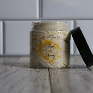 K&ouml;nnte beinhalten: Ein transparentes Glas mit wei&szlig;er, geschlagenem K&ouml;rperbutter mit einem gelben und wei&szlig;en Etikett, auf dem "Whipped Soap Co. Oatmeal & Honey Whipped Body Butter 2 oz / 57 grams" steht. Das Glas ist offen und der Deckel ist schwarz.