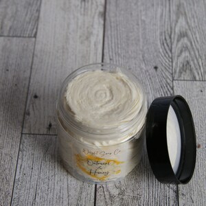 K&ouml;nnte beinhalten: Ein klares Glas mit einem wei&szlig;en Deckel, gef&uuml;llt mit einer wei&szlig;en Creme. Das Glas hat ein Etikett mit der Aufschrift "Wright Soap Co. Oatmeal & Honey".