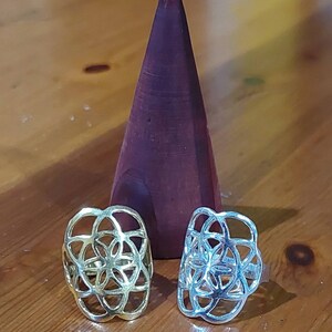 Puede incluir: Dos anillos de plata con un dise&ntilde;o de flor geom&eacute;trico. Los anillos est&aacute;n sobre una superficie de madera.