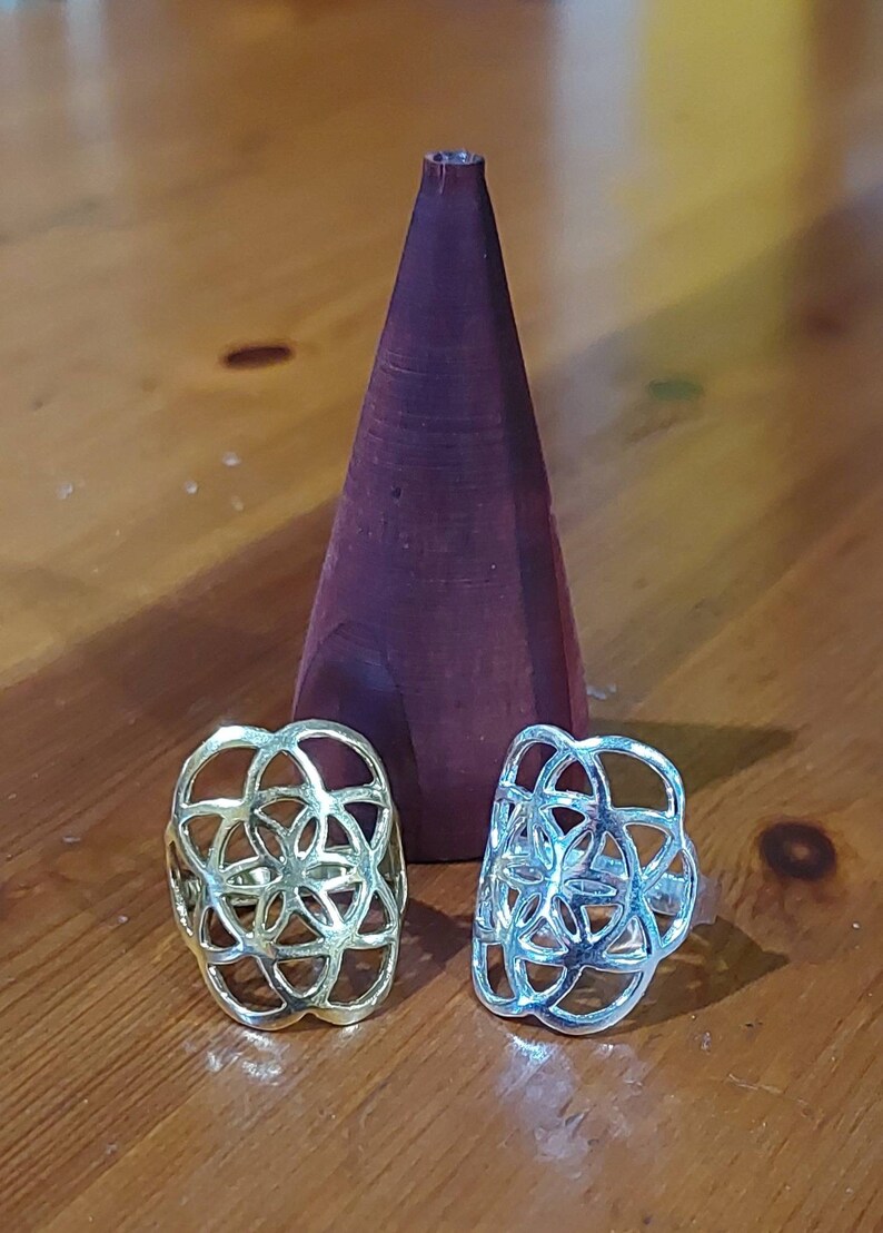 Puede incluir: Dos anillos de plata con un dise&ntilde;o de flor geom&eacute;trico. Los anillos est&aacute;n sobre una superficie de madera.