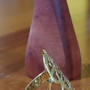 Puede incluir: Un anillo de oro con un dise&ntilde;o delicado e intrincado que se asemeja a un &aacute;rbol o una flor estilizados. El anillo est&aacute; sobre una superficie de madera.