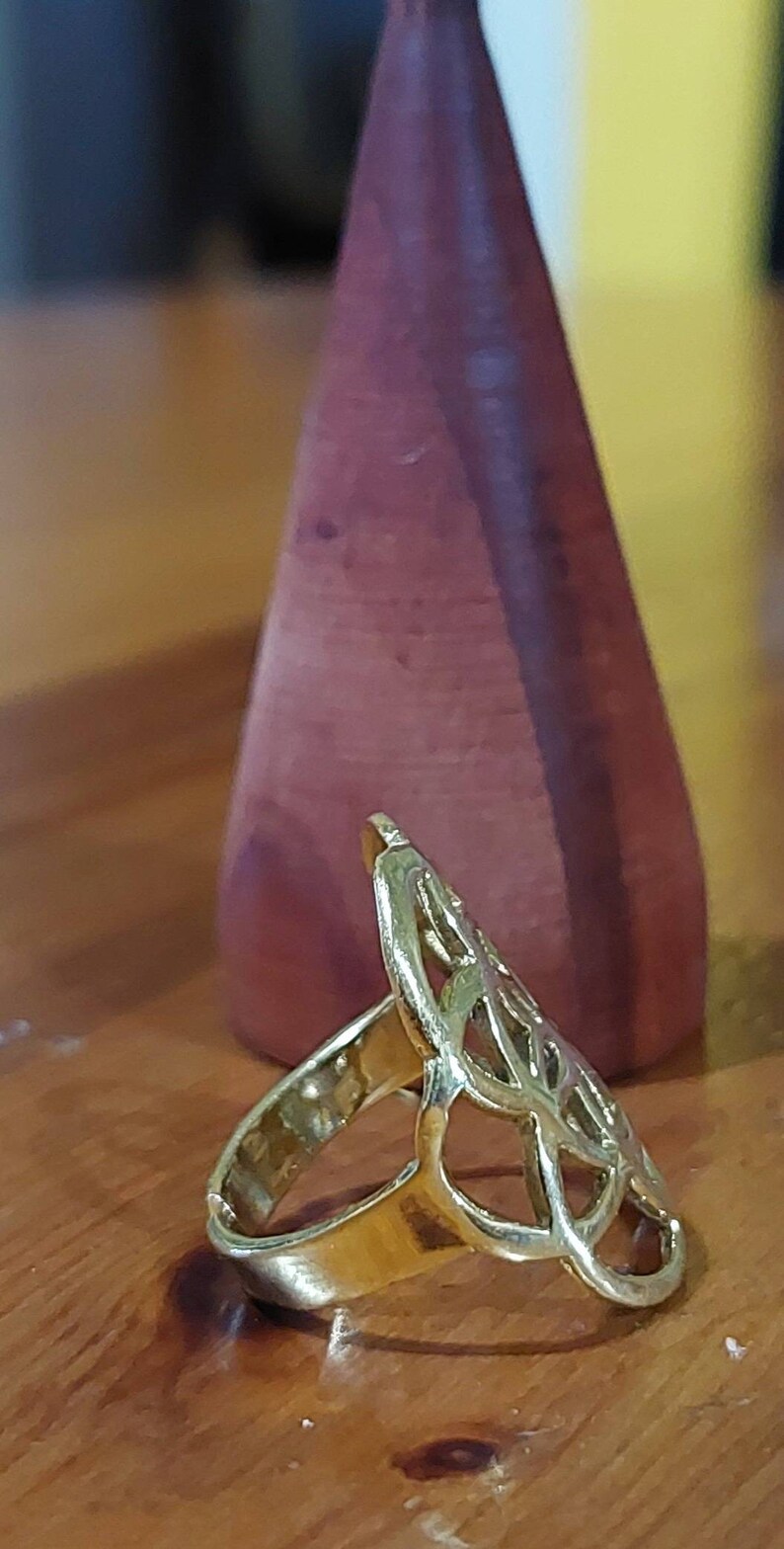 Puede incluir: Un anillo de oro con un dise&ntilde;o delicado e intrincado que se asemeja a un &aacute;rbol o una flor estilizados. El anillo est&aacute; sobre una superficie de madera.