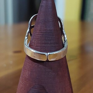 Puede incluir: Un anillo de plata con un dise&ntilde;o geom&eacute;trico. El anillo se muestra en un soporte de anillo de madera.