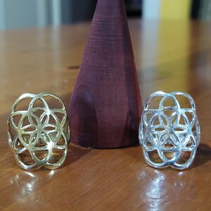 Puede incluir: Dos anillos de plata con un dise&ntilde;o de flor geom&eacute;trico. Los anillos est&aacute;n sobre una superficie de madera.