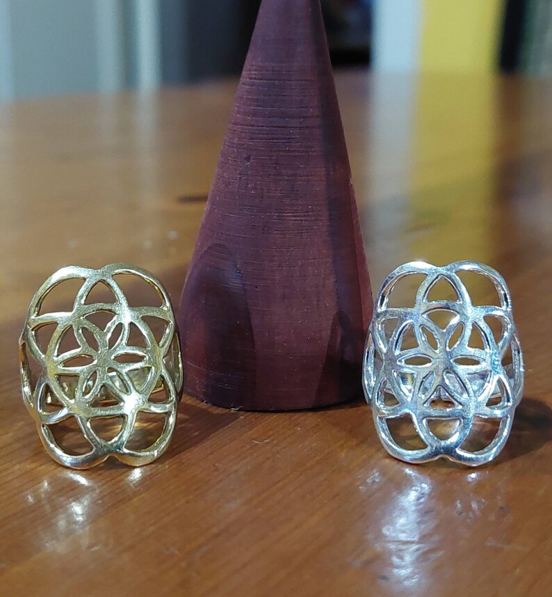 Puede incluir: Dos anillos de plata con un dise&ntilde;o de flor geom&eacute;trico. Los anillos est&aacute;n sobre una superficie de madera.