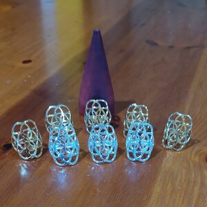 Puede incluir: Siete anillos de metal de color dorado con un dise&ntilde;o geom&eacute;trico. Los anillos est&aacute;n dispuestos en semic&iacute;rculo sobre una superficie de madera.