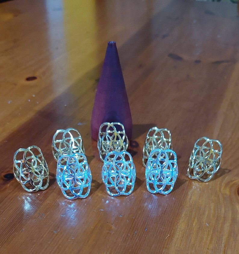 Puede incluir: Siete anillos de metal de color dorado con un dise&ntilde;o geom&eacute;trico. Los anillos est&aacute;n dispuestos en semic&iacute;rculo sobre una superficie de madera.