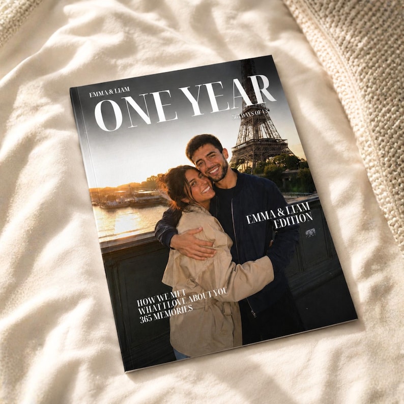 K&ouml;nnte beinhalten: Ein personalisiertes Fotobuch mit dem Titel ONE YEAR und dem Untertitel 365 DAYS OF US. Das Cover zeigt ein Foto von zwei Personen, die sich vor dem Eiffelturm bei Sonnenuntergang umarmen. Der Text umfasst EMMA & LIAM, EMMA & LIAM EDITION, HOW WE MET, WHAT I LOVE ABOUT YOU und 365 MEMORIES.