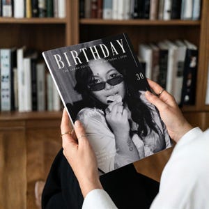 Puede incluir: Una persona sostiene una revista en blanco y negro titulada "BIRTHDAY". La portada presenta a una mujer con gafas de sol y el número "30". El texto dice "THE SARAH EDITION | 30TH BIRTHDAY | 2026" y "30 & THRIVING".