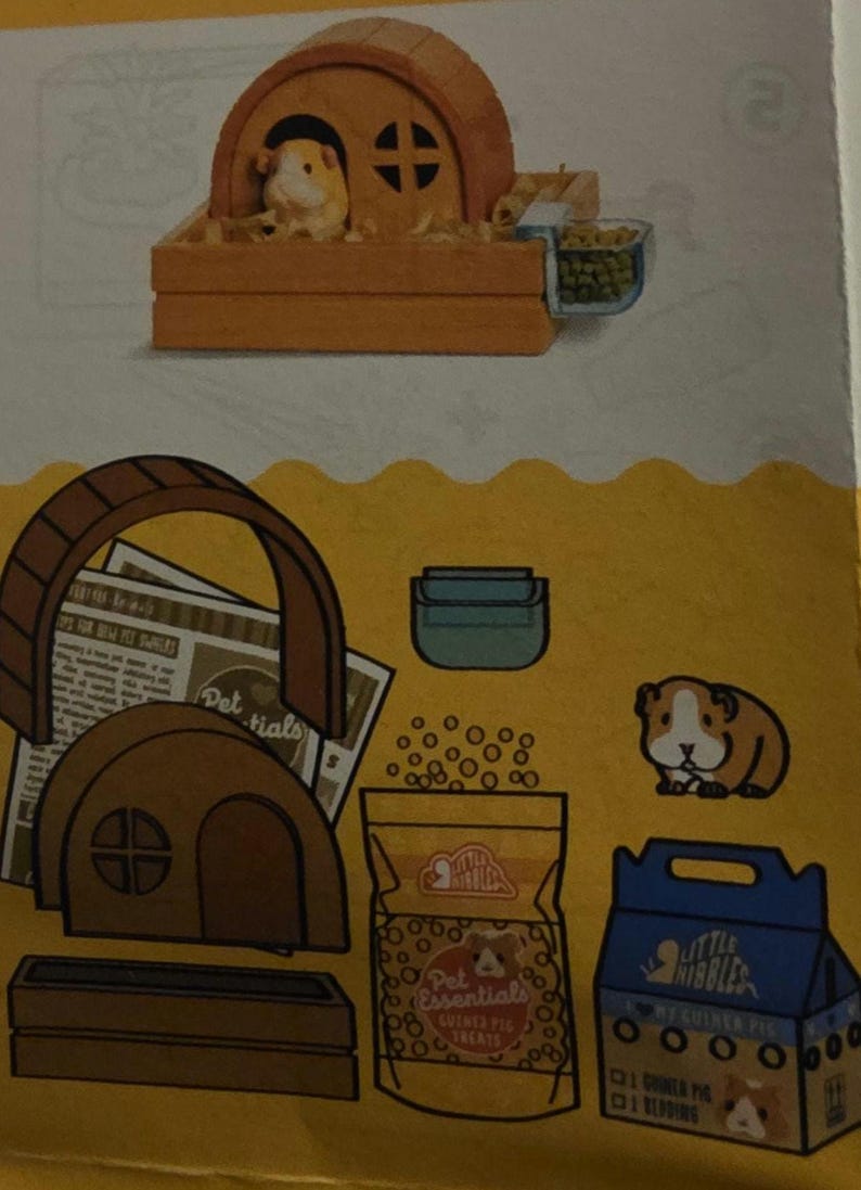 May include: An illustration of guinea pig accessories, including a wooden house, a wheel, food, and a carrier. The image features a guinea pig inside the house. The packaging reads "Pet Essentials Guinea Pig Treats" and "Little Nibbles".