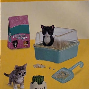 May include: A miniature set featuring a black and white kitten in a blue litter box, a grey tabby kitten, a pink bag of cat litter labeled LITTER-ALLY THE BEST, a blue scoop, and a small white planter with a cat face and green grass.