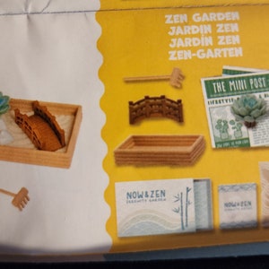 May include: A miniature Zen garden kit with a wooden tray, bridge, rake, and succulent. The kit includes a small newspaper with the text "THE MINI POST" and "LIFESTYLE & Birds". The packaging features the text "NOW & ZEN".