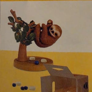 May include: A brown sloth figurine hanging from a tree branch on a circular base, accompanied by small blue and white spherical objects. A small open cardboard box containing similar spherical items sits nearby on a yellow background with text.
