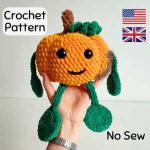 May include: A crochet pumpkin amigurumi toy with a smiling face, green leaves, and brown stem. The toy is held in a hand and the text "No Sew" is visible in the image.