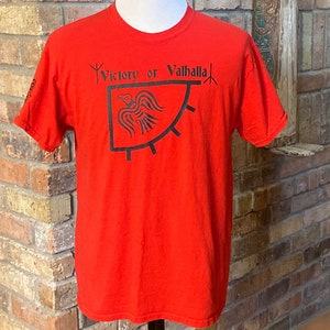 Könnte beinhalten: Rotes T-Shirt mit einer schwarzen Grafik eines Rabens und dem Text "Victory or Valhalla".
