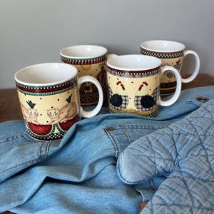 May include: Four ceramic mugs with white interiors and handles. Two mugs feature illustrations of tan cats with black birds, while the other two display images of chickens. All mugs have a cream-colored background with a checkered border pattern.